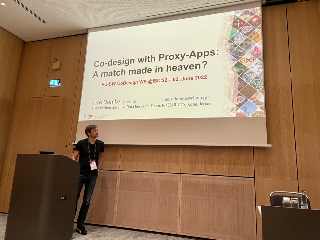 Presenter in front of the wall with the presentation slide "Co-Design with Proxy Apps: A match made in heaven?"
