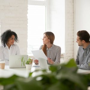 Multiracial male and female colleagues discussing document at team meeting or corporate office briefing, diverse friedly african and caucasian partners talking about contract at group negotiations